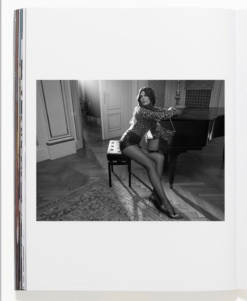 Woman in leopard print top and leather shorts sits near piano in interior setting, captured in a black and white photograph on a book page.