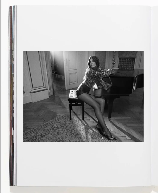 Woman in leopard print top and leather shorts sits near piano in interior setting, captured in a black and white photograph on a book page.