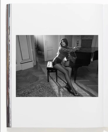 Woman in leopard print top and leather shorts sits near piano in interior setting, captured in a black and white photograph on a book page.