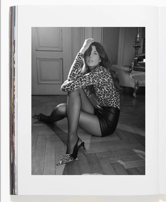 Monochrome fashion portrait of a model seated on a parquet floor wearing a leopard print top and slingback heels