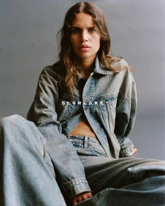 Model seated wearing a distressed denim jacket and matching jeans against a solid grey background for Slvrlake denim lookbook.