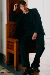 Model Tim Schuhmacher seated on an ornate wooden chair in a dark suit for Massimo Dutti