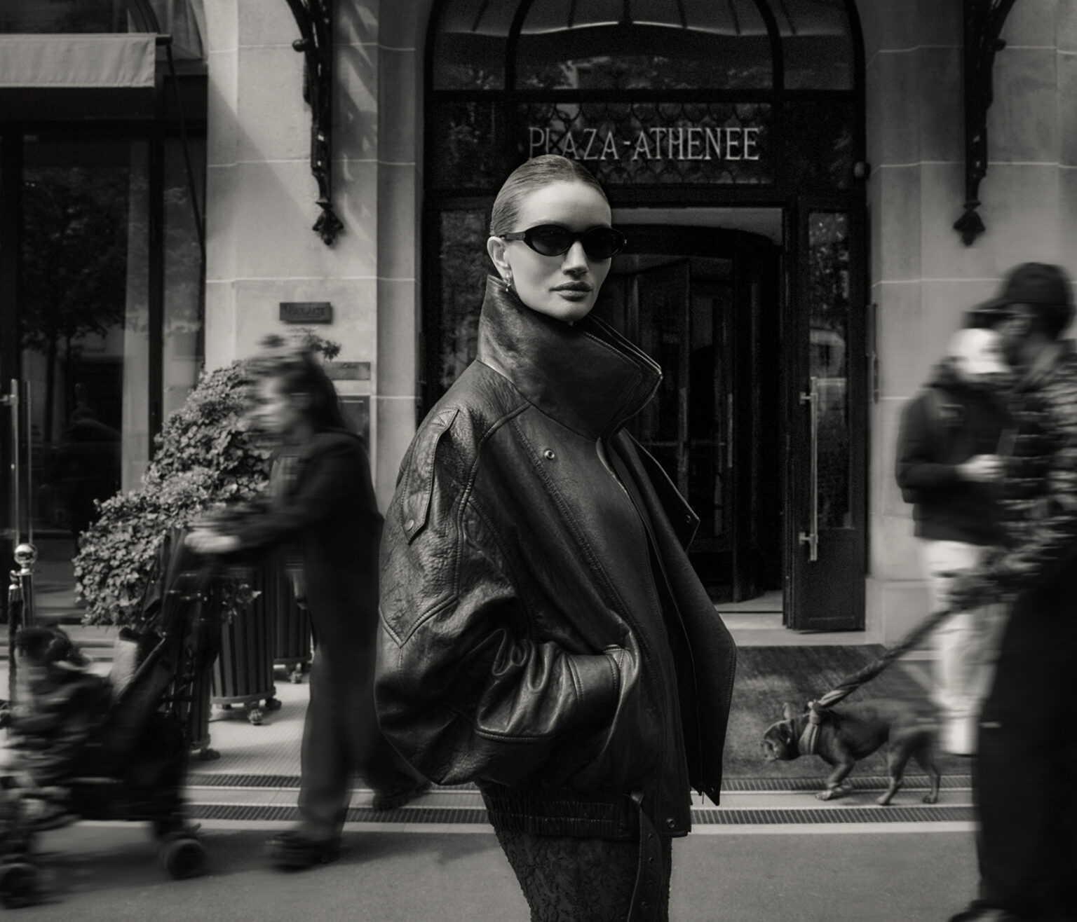 Model in sunglasses and dark leather jacket standing outside Plaza Athenee with blurred pedestrians