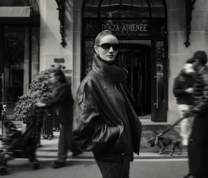 Model in sunglasses and dark leather jacket standing outside Plaza Athenee with blurred pedestrians