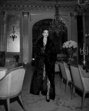 Model wearing a long dark fur coat standing inside an opulent dining room for Harper's Bazaar Australia