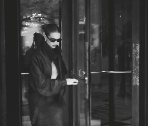 Woman in dark sunglasses and leather jacket opening a glass hotel door