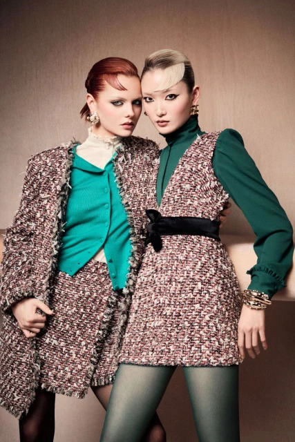 Two fashion models pose indoors wearing tweed skirt suits, one in green tights, showcasing a blend of textures and colors.