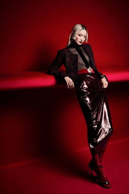 Fashion shot of an Asian woman with platinum blonde hair posing in a dark red outfit in a studio setting with red background.
