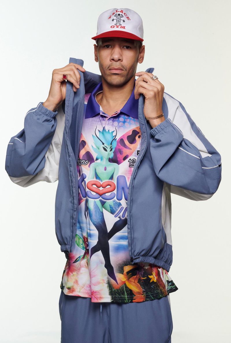 Portrait of a stylish adult male in athletic wear and a baseball cap. He has his hands raised near his neck.