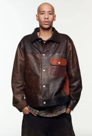 Adult male in a distressed brown leather jacket and black pants poses in front of a white backdrop in a studio setting.