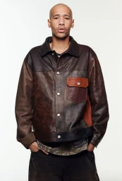 A bald man wearing a brown multi-tone leather jacket with front pockets against a plain white studio backdrop.