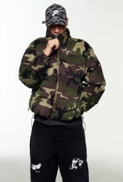Model wearing a camouflage puffer jacket and printed cap against a white background for Palace Spring 2025