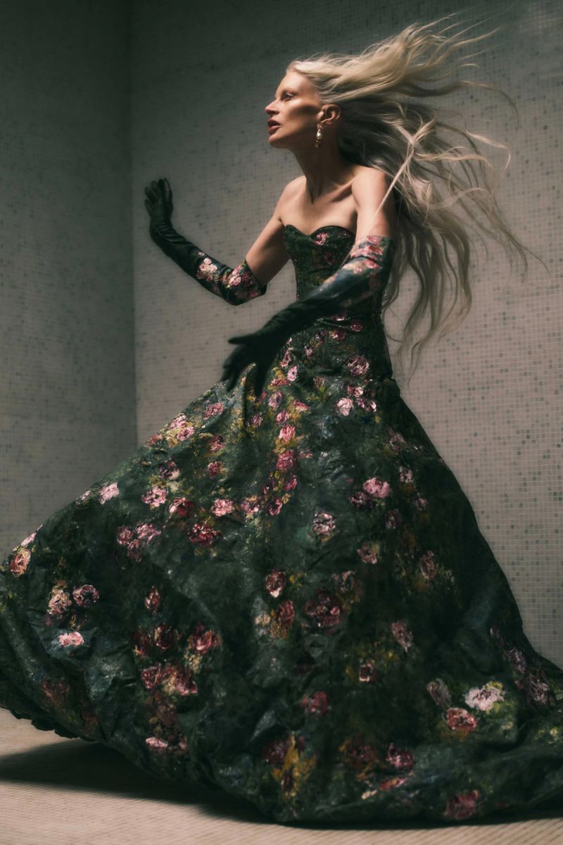 A woman with flowing blonde hair and dark floral dress posing in an abstract space, capturing a blend of fashion and art.