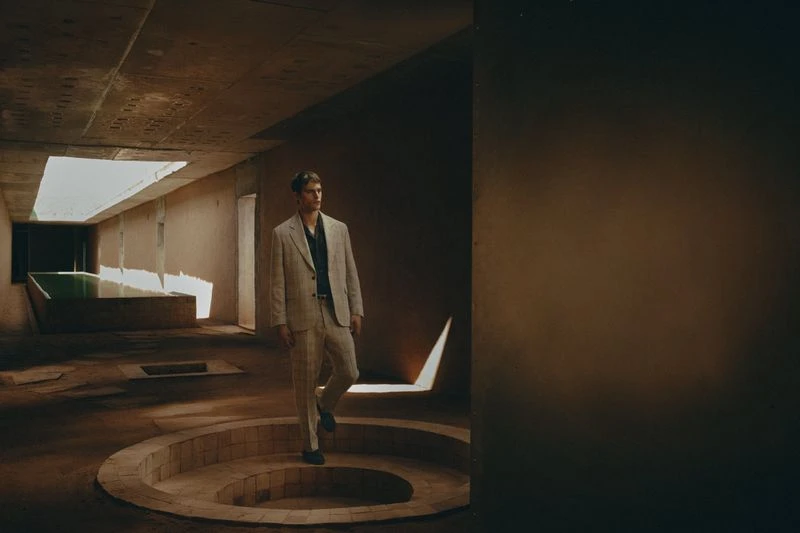 A man in a suit walks down steps inside a modern concrete building with large open skylights for natural lighting.