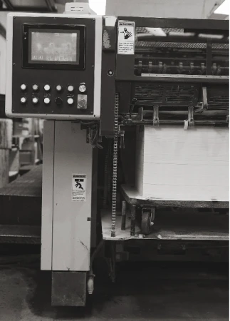Industrial printing machinery showing the control panel, paper feed, warning labels, metal components, and various mechanical elements.