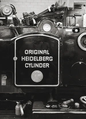 Close-up black and white photograph of an industrial Heidelberg printing press with the embossed text Original Heidelberg Cylinder.
