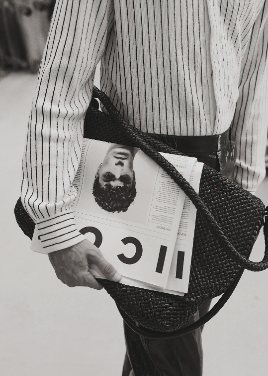 Striped shirt, woven bag, and magazine with a man's portrait create a stylish monochrome image focused on fashion and accessories.