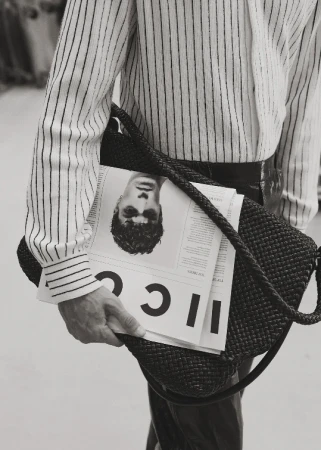 Striped shirt, woven bag, and magazine with a man's portrait create a stylish monochrome image focused on fashion and accessories.