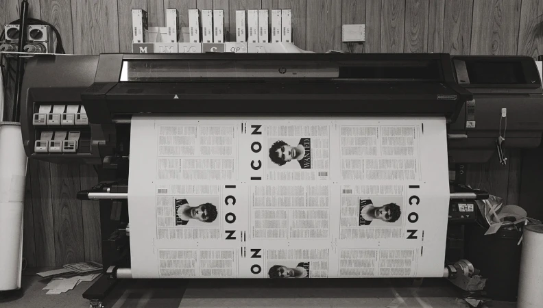 A black-and-white photograph shows a large-format printer outputting pages with 'ICON' and a man's portrait, against a wood-panel wall.