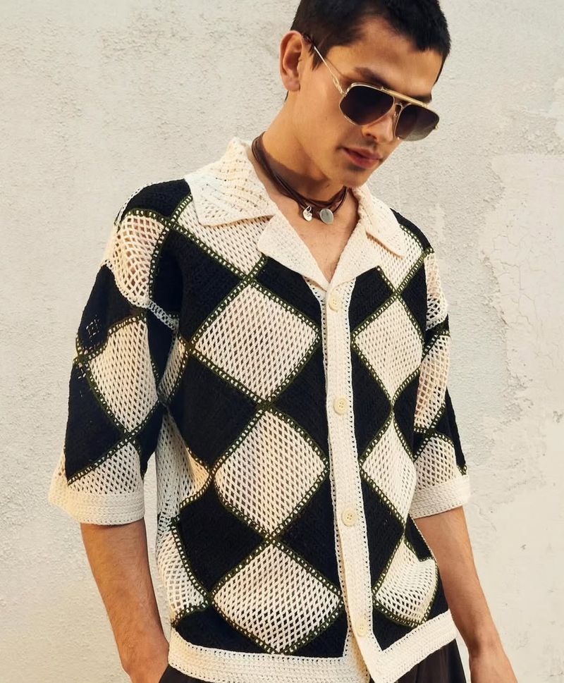Man wearing a black and off-white diamond pattern knitted shirt with aviator sunglasses posing against a textured neutral background.
