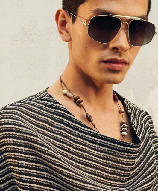 Close-up of a stylish adult male wearing aviator sunglasses and a beaded necklace, showcasing fashion and personal style.