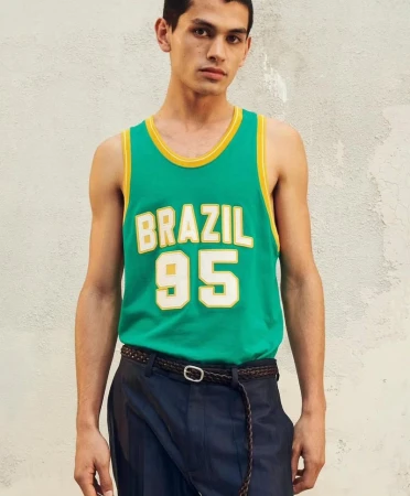 A young male model wearing a green tank top with yellow trim and Brazil 95 lettering against a textured neutral background