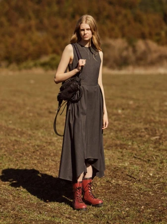 Model in a dark grey midi dress and red lace-up boots standing in a grassy meadow under natural sunlight.