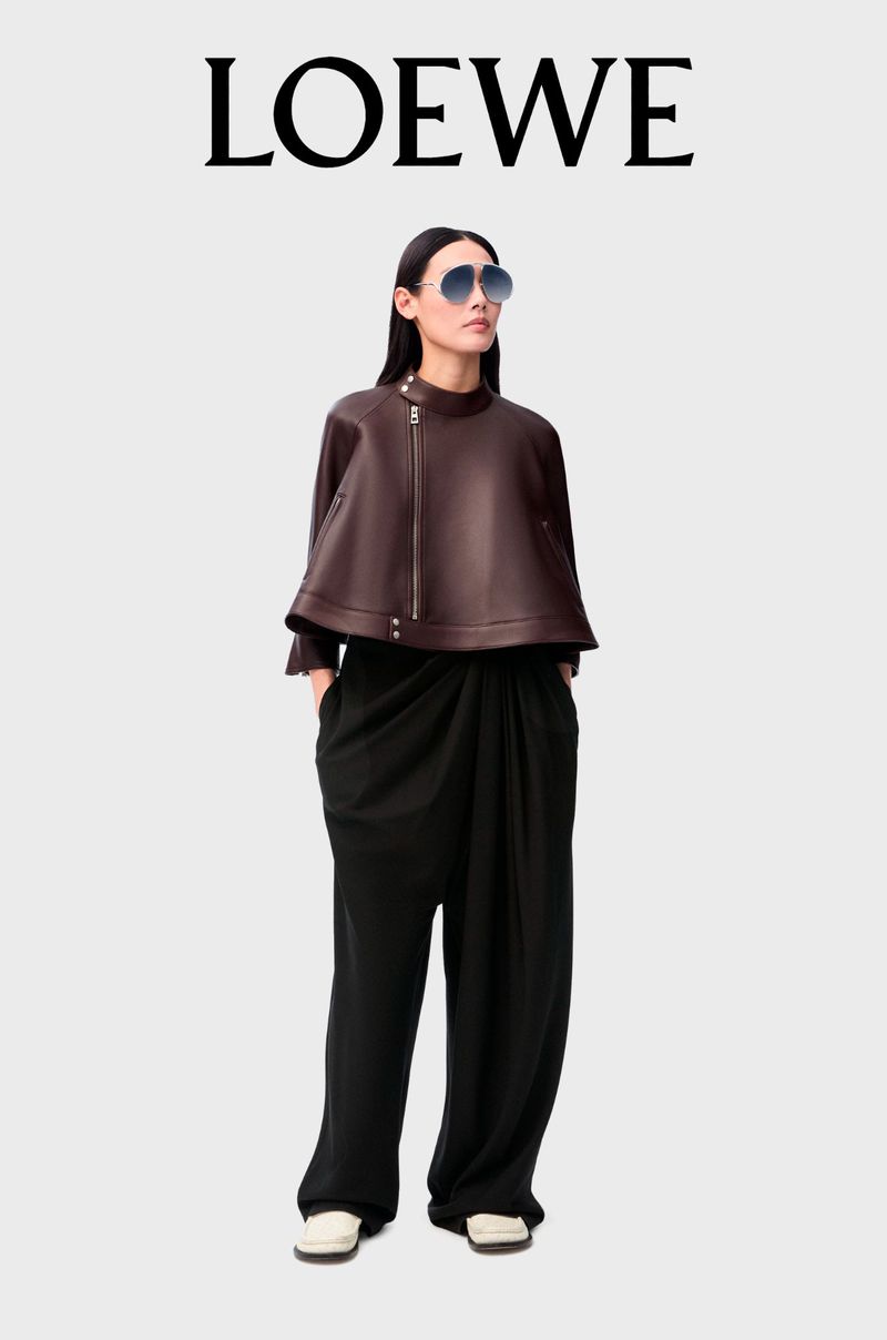 Fashionable woman wearing a brown asymmetrical jacket and black pants, posing against a white background with LOEWE text overhead.