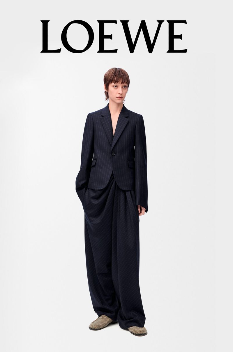An adult female fashion model wears a pinstripe suit and tan shoes in a studio shot for Loewe fashion brand promotion. 