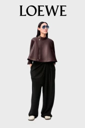 Model wearing oversized brown leather top and black trousers against plain white background