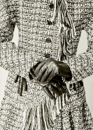 Close-up studio shot of a tweed skirt suit with button closure, fringe, and black leather gloves, creating a chic fashion ensemble.