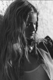 Portrait of a woman with long wavy hair wearing a denim jacket against a textured wall