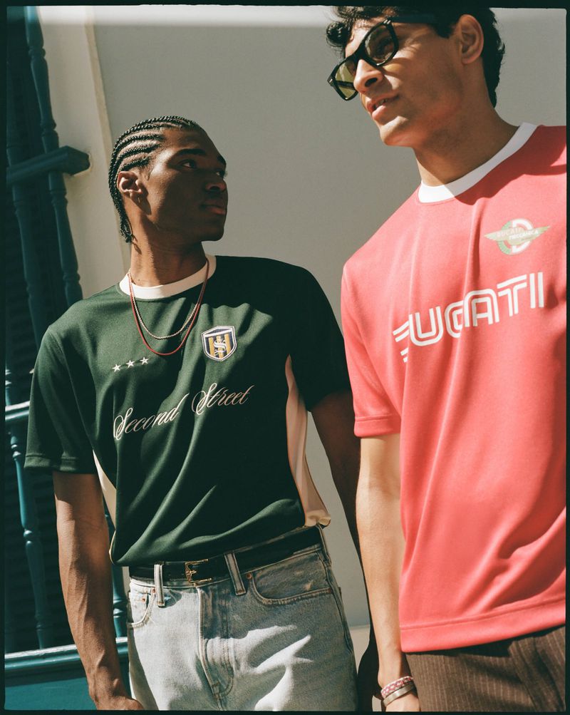 Two male models posing outdoors wearing graphic sports jerseys and jeans for Abercrombie and Fitch.