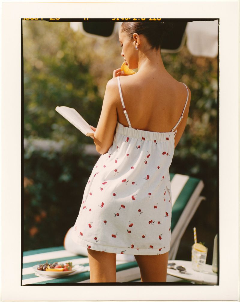 Woman in a white summer dress with cherries, enjoying fruit by the pool, reading a book on a sunny day. Relaxing poolside.