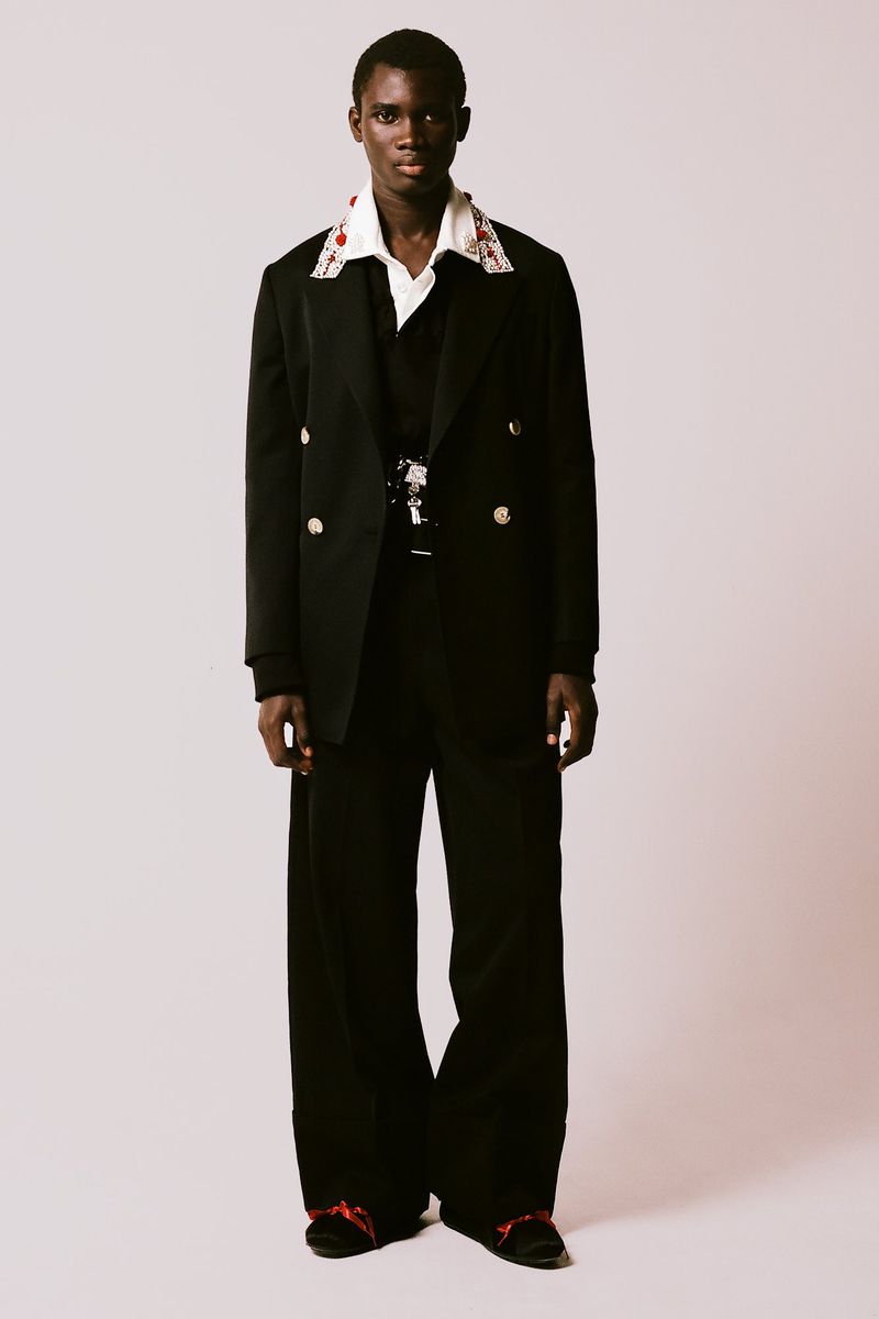 Full-length portrait of a Black male model in a black suit with white shirt and wide-legged trousers on a clean background.