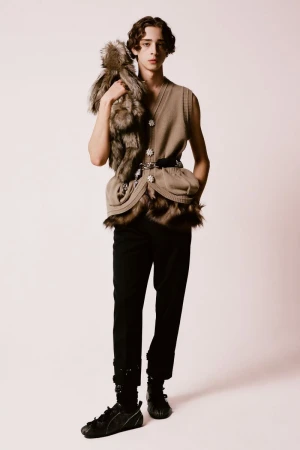 Full-length studio portrait of a young man in a sleeveless tan top and black pants, carrying a fur pelt over his shoulder.