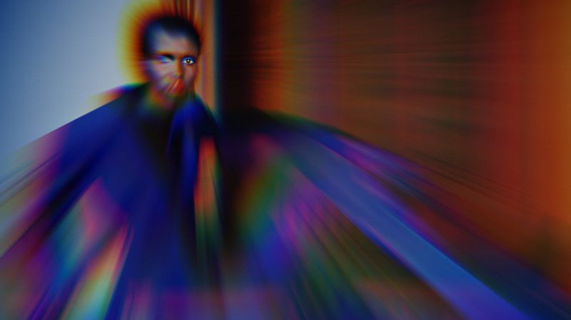 Portrait of an African American adult with intense stare and colorful visual effects, blurred background, and mysterious mood.