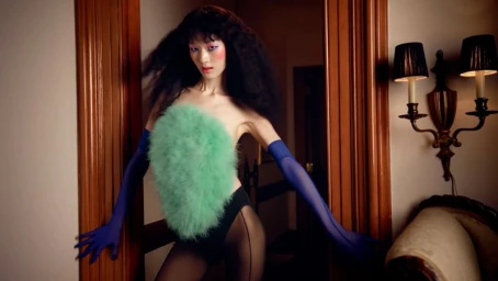 Model in green feather top and blue gloves posing in a doorway for Mugler Fall/Winter 2025 campaign