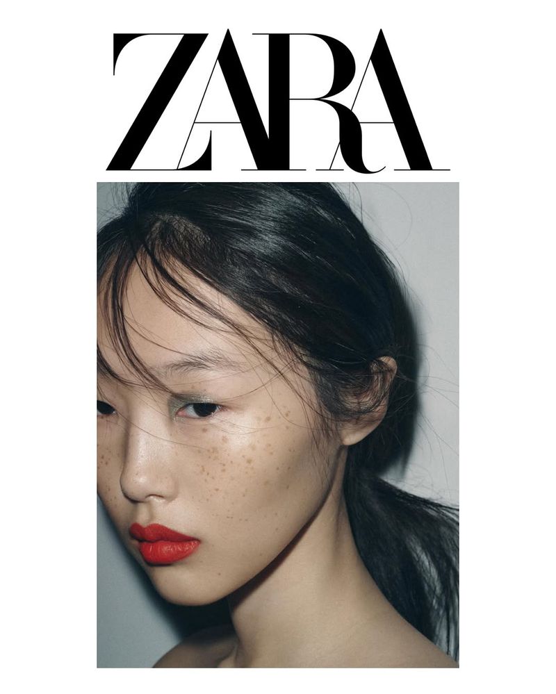 Close-up portrait of a young adult Asian woman with dark hair in a ponytail, red lipstick, and visible freckles, next to the Zara logo.