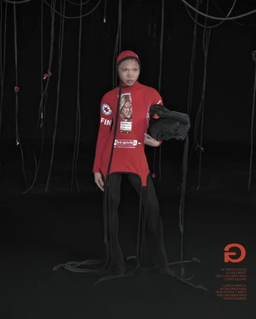 Fashion model in red long-sleeve shirt with attached leggings poses indoors with hanging cords and a black accessory bag.