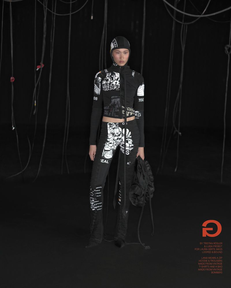 Fashion photo of a woman posing in a black printed jacket and pants ensemble with a matching hat, set against a dark background.