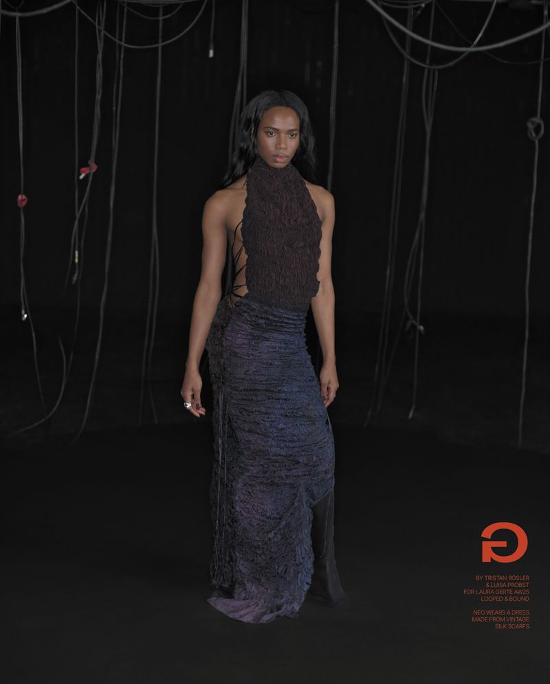 Woman in textured sleeveless gown in studio setting with black background and hanging cables in fashion photography.