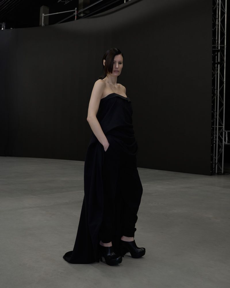 Adult female in an all-black strapless top and wide leg pants poses in a photo studio with a black backdrop and light grey floor.