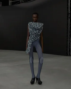 Model wearing a structured plaid top and patterned grey leggings in a dark studio setting for Sia Arnika AW25