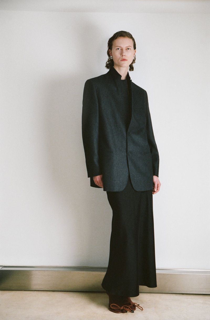 Model standing against a white seamless background wearing a dark tailored blazer and long black skirt from Petar Petrov.