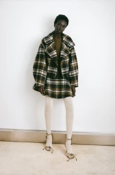 Model wearing a plaid jacket and matching skirt with light tights against a white backdrop