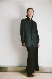 Model standing against a white seamless background wearing a dark tailored blazer and long black skirt from Petar Petrov.