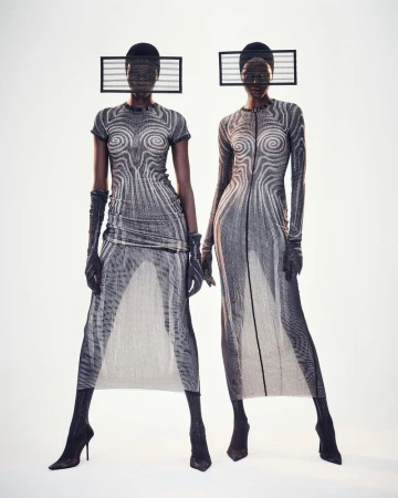 Two Black female fashion models pose in gray-patterned gowns with geometric headwear against a bright background in a studio shot.