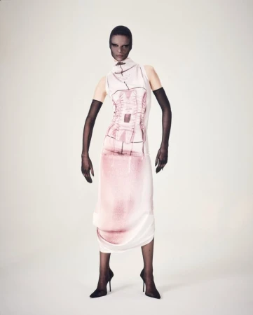 Fashion shot of a slender adult female wearing a high neck, sleeveless pink and white dress with black heels and arm gloves in a studio.