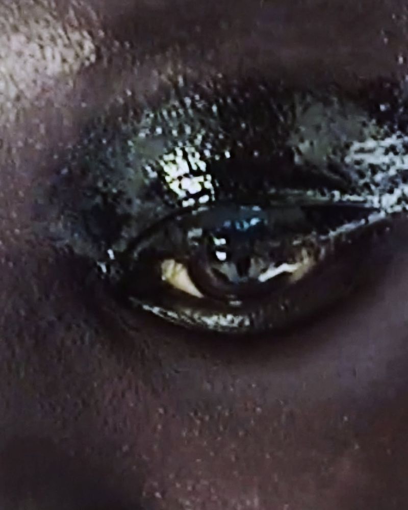 Extreme close-up of a human eye with dramatic, glossy black eyeshadow and subtle white eyeliner highlighting the lower lash line.